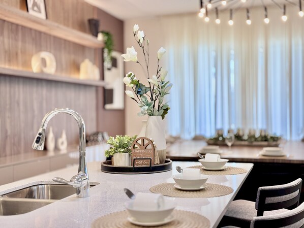 Ett modernt kök med en diskho i rostfritt stål, en vas med blommor och en matplats med ett bord dukat för två personer.