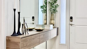 Un couloir avec une console en bois, un miroir, un vase contenant des plantes vertes et une porte dotée d’un clavier pour l’ouverture à code.