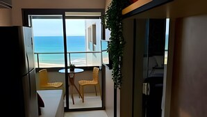 Una cocina moderna con vistas a la playa, un comedor con mesa y sillas, y un pequeño balcón con una silla.