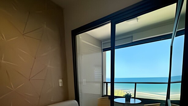 Una sala de estar moderna con sofá y puerta de vidrio que da a un balcón con vista a la playa.
