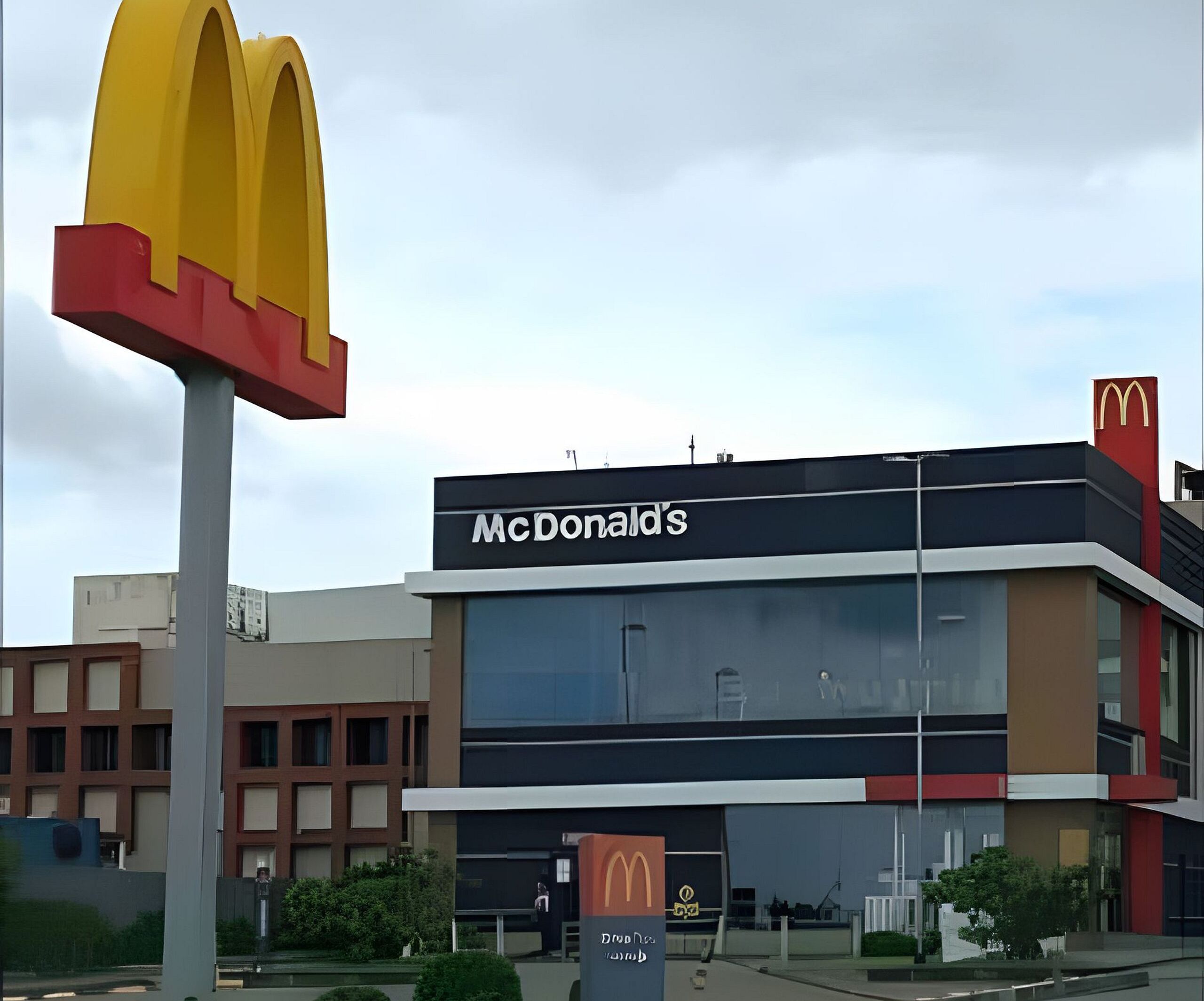 Um restaurante McDonald's com um grande letreiro amarelo e vermelho, arquitetura moderna e céu claro.