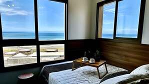 Un dormitorio con una cama, una mesita de noche con tazas y vistas al océano a través de amplias ventanas.