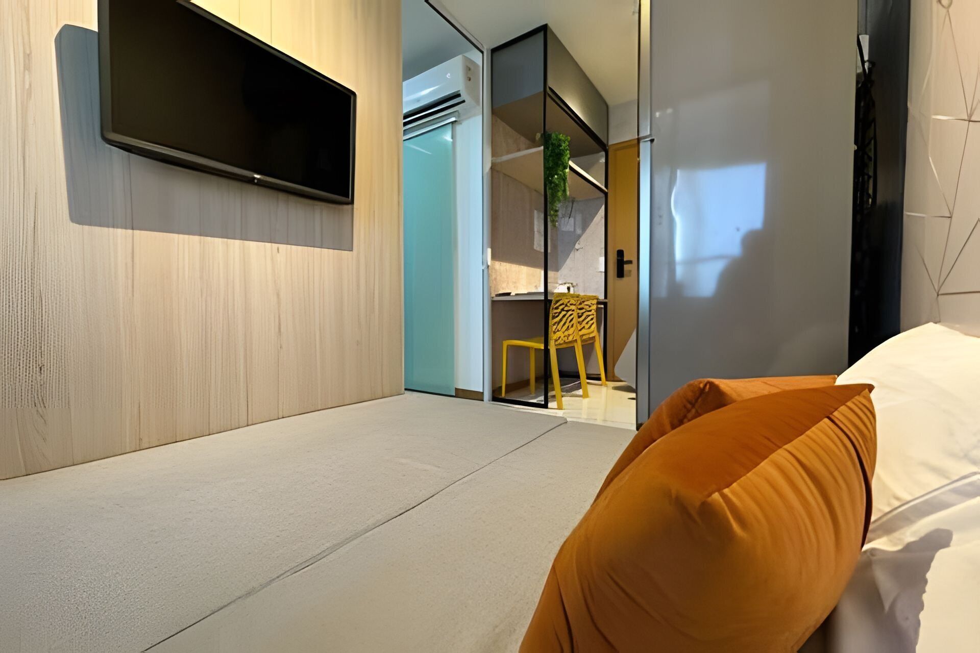 Une chambre d’hôtel moderne équipée d’un lit, d’un téléviseur à écran plat fixé au mur, d’un petit bureau avec une chaise et d’une porte coulissante donnant accès à la salle de bain.