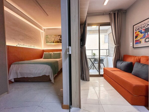 A modern bedroom with a bed, a sofa, and a balcony with a table and chairs.