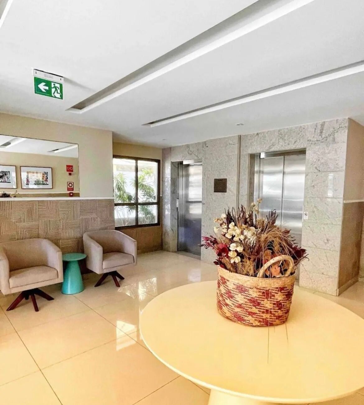 A lobby with a round table, two armchairs, a decorative basket, and two elevators.