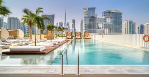 A rooftop pool with lounge chairs and palm trees, overlooking a city skyline with modern buildings. - Prime Location Pristine Studio in Business Bay (Dubai)