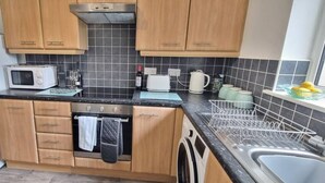 A compact kitchen with wooden cabinets, a microwave, a kettle, and a dish rack. - The Pennington Apartment Leigh (Leigh)