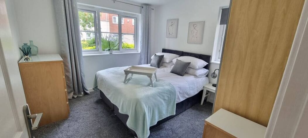 A bedroom with a bed, bedside tables, a window, and a view of the outside.