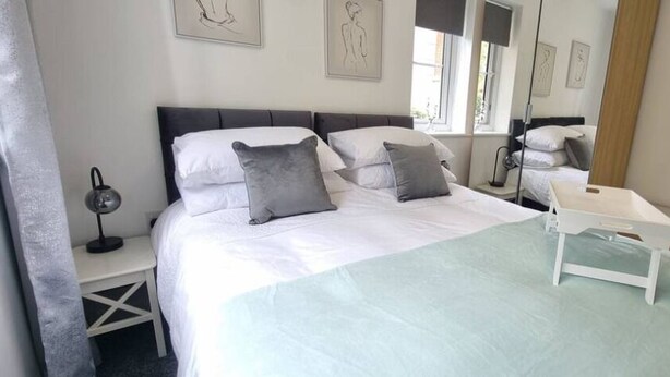A neatly arranged bedroom with a large bed, bedside tables, and a bedside lamp. - The Pennington Apartment Leigh (Leigh)