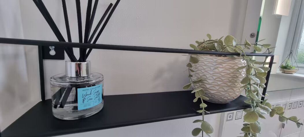 Uno scaffale con una bottiglia trasparente di diffusore di fragranze Hotel Collection e una pianta in vaso decorato.