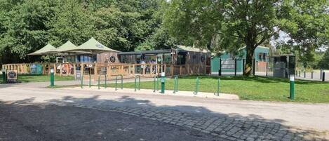 A wooden structure with a green roof, possibly a café or restaurant, surrounded by a fence and trees.