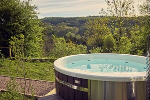 Un jacuzzi en un jardín con vistas a una colina boscosa.