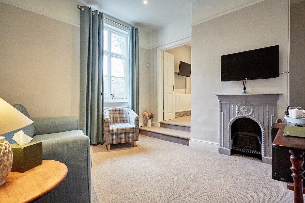 A living room with a sofa, armchair, fireplace, television, and a window with curtains.