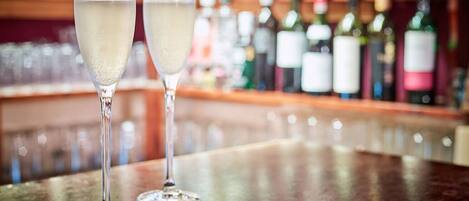 Two champagne flutes on a bar counter with a blurred background of bottles.