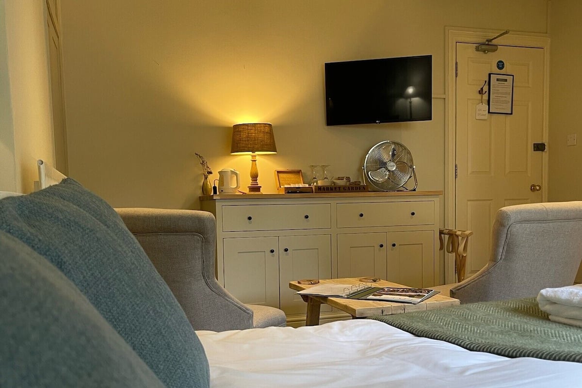 A hotel room with a bed, a desk, a chair, a television, and a door with a sign.