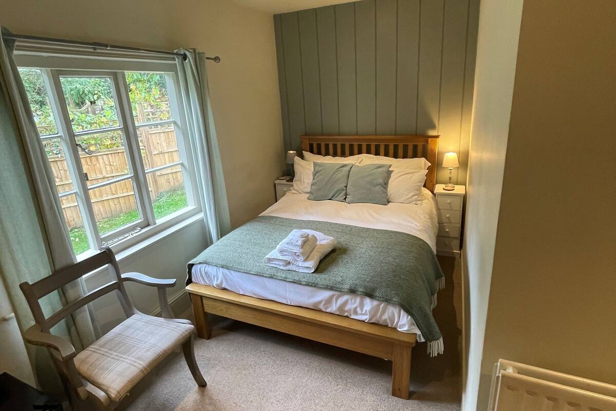 A bedroom with a bed, a chair, a nightstand, a lamp, and a window.