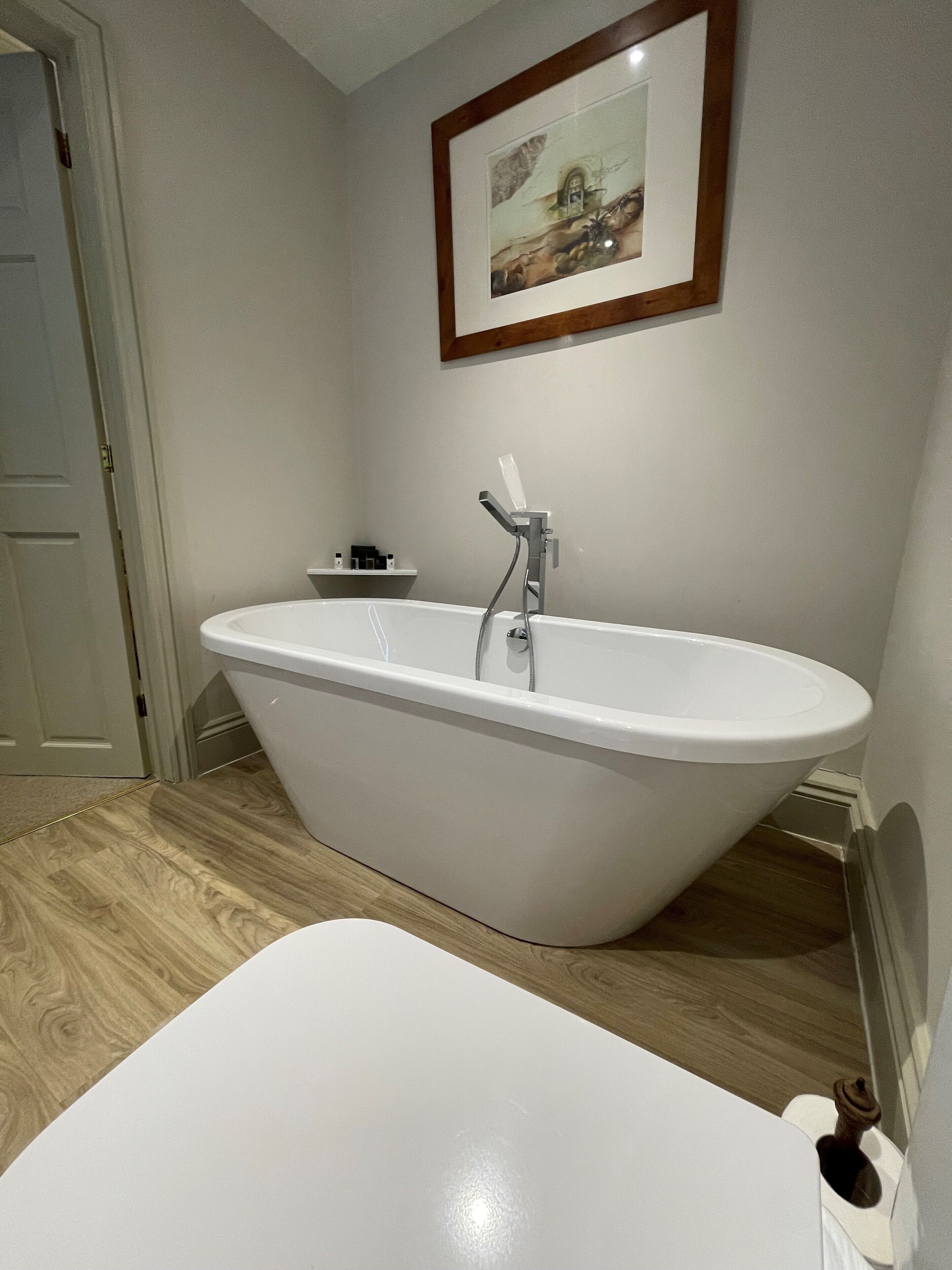 A bathroom with a freestanding bathtub, a toilet, and a framed picture on the wall.