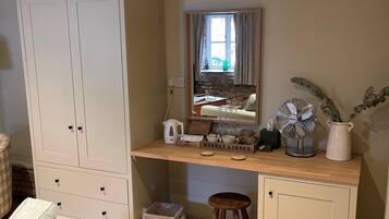 Een kamer met een grote witte garderobe, een houten bureau met een spiegel, een klein krukje en een rieten mand.