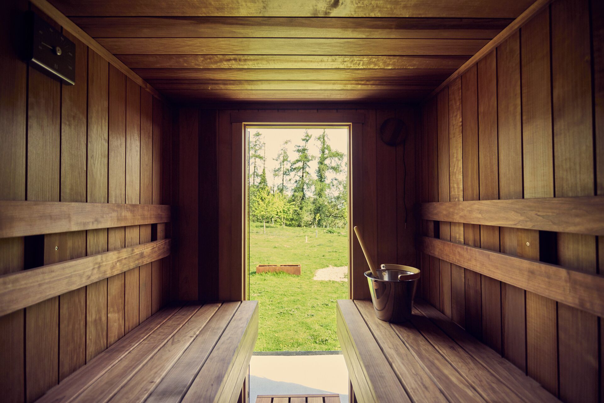 A sauna room with wooden benches and a bucket of water.