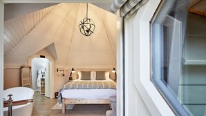 Ein Schlafzimmer mit schrägen Wänden, einem Bett mit gestreifter Bettdecke, Nachttischlampen und einer Hängelampe.