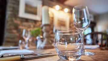 A dining table with a clear glass, a pen, and a candle in a cozy, warmly lit room with a brick wall and framed picture.
