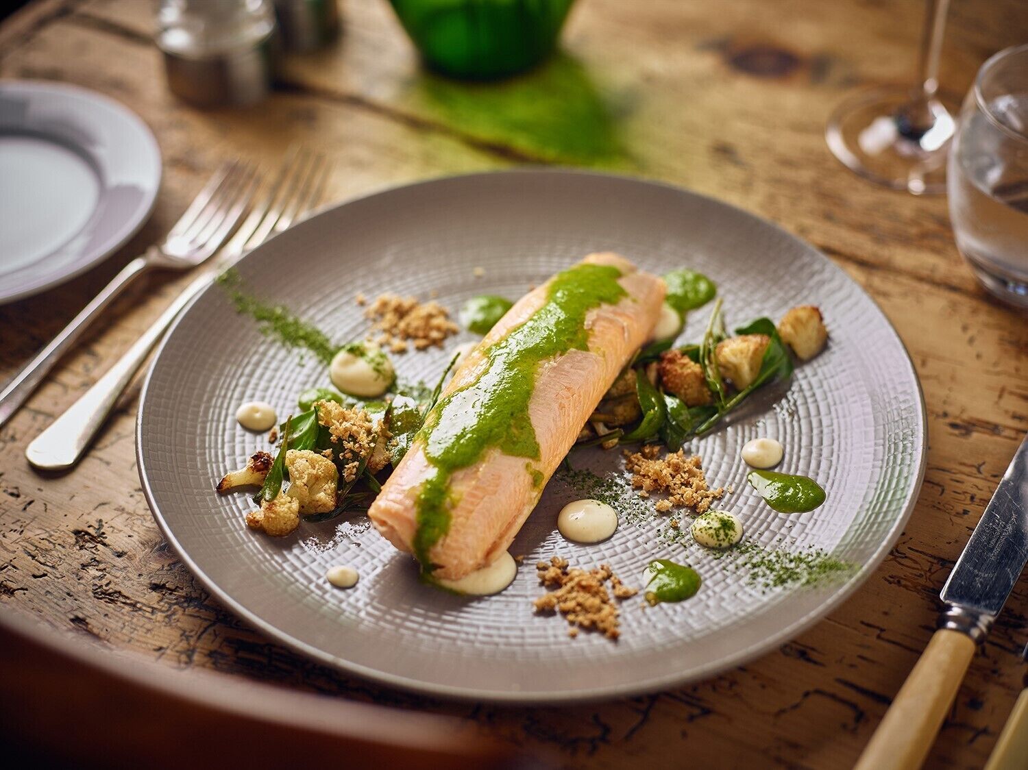 Un plato con un rollo de pescado, posiblemente salmón, acompañado de vegetales verdes y cubitos de pan.