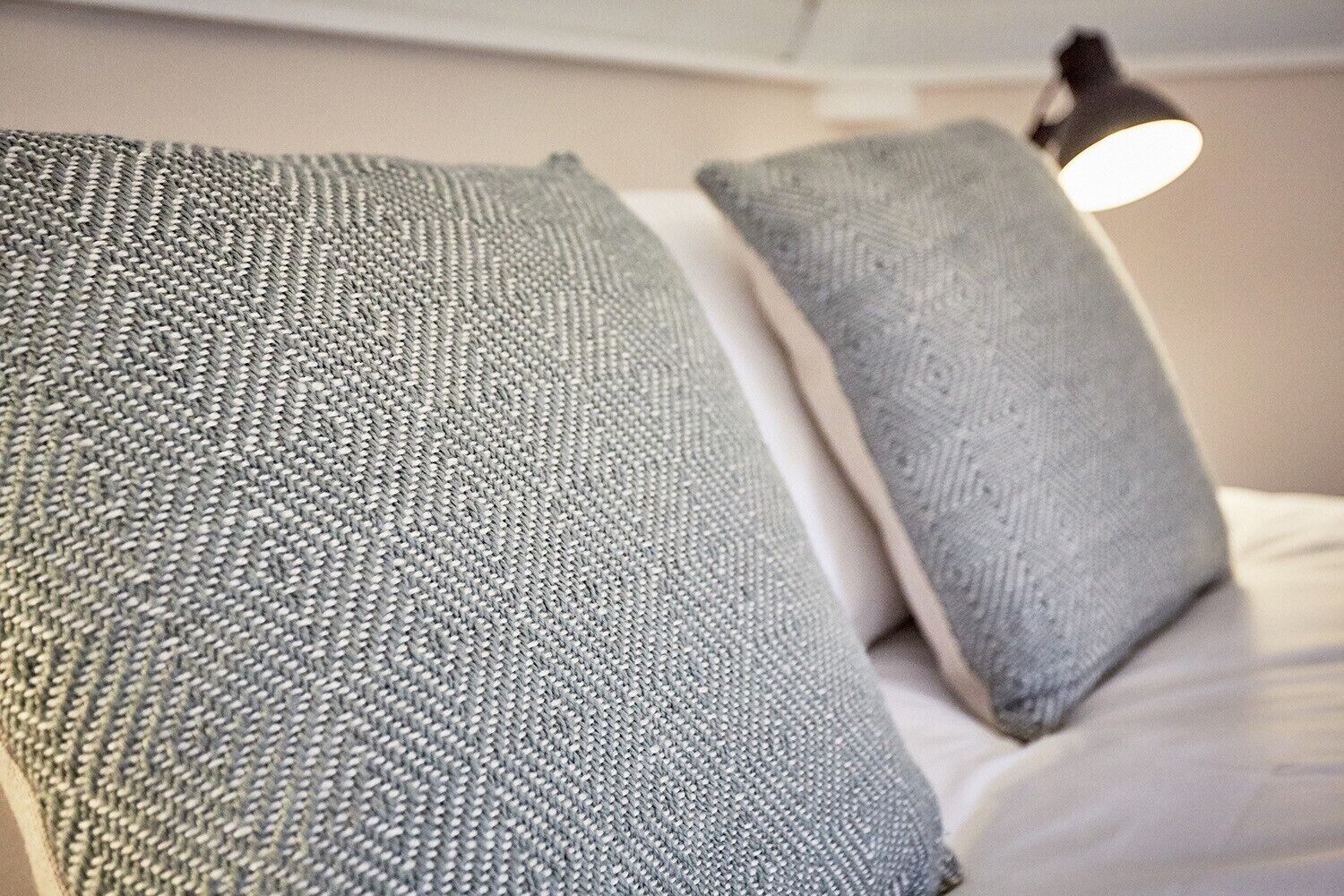 A close-up of a bed with grey textured pillows and a bedside lamp.