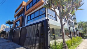 Un edificio moderno a più piani con ampie finestre, un ingresso con cancello e una palma in primo piano.