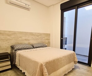 A bedroom with a bed, a nightstand, a wall-mounted air conditioner, and a sliding glass door to a balcony. - Casa Carmel (Torres)
