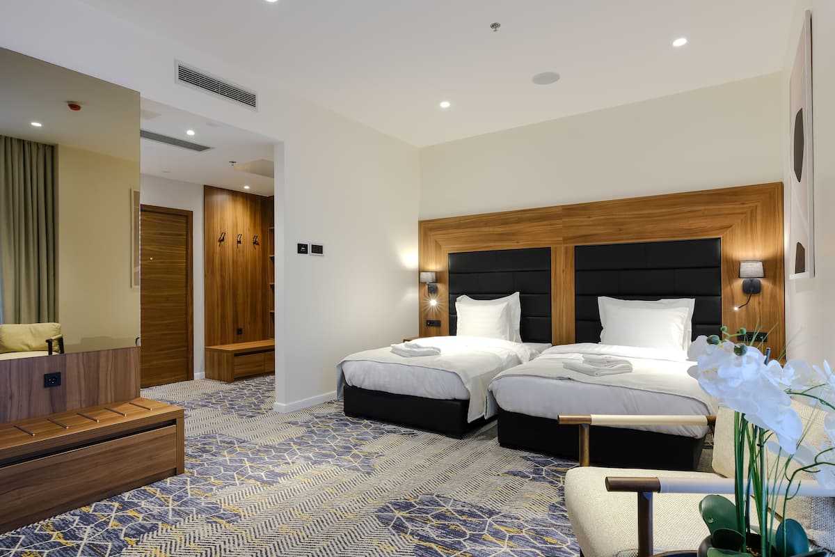 A hotel room with two beds, a desk, a chair, and a large mirror.