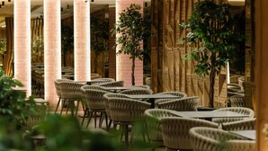 A restaurant with round tables and cushioned chairs, surrounded by tall columns and decorative panels.