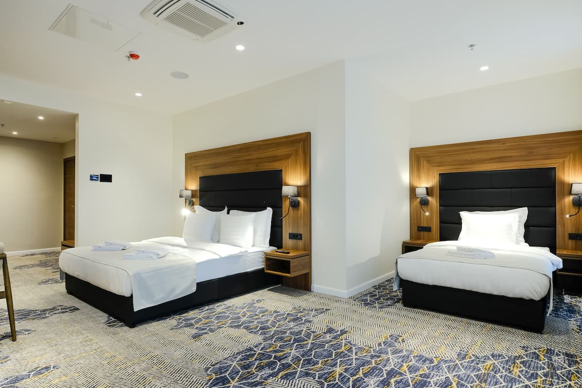 A hotel room with two beds, each with a wooden headboard, bedside tables, and a patterned carpet.