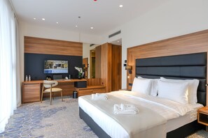 A modern hotel room with a large bed, a desk with a chair, a television, and a mirror. - Hotel Vema (Visoko)