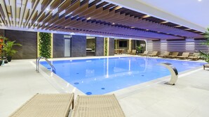 An indoor swimming pool with a modern design, including a wooden ceiling and lounge chairs around the pool area.