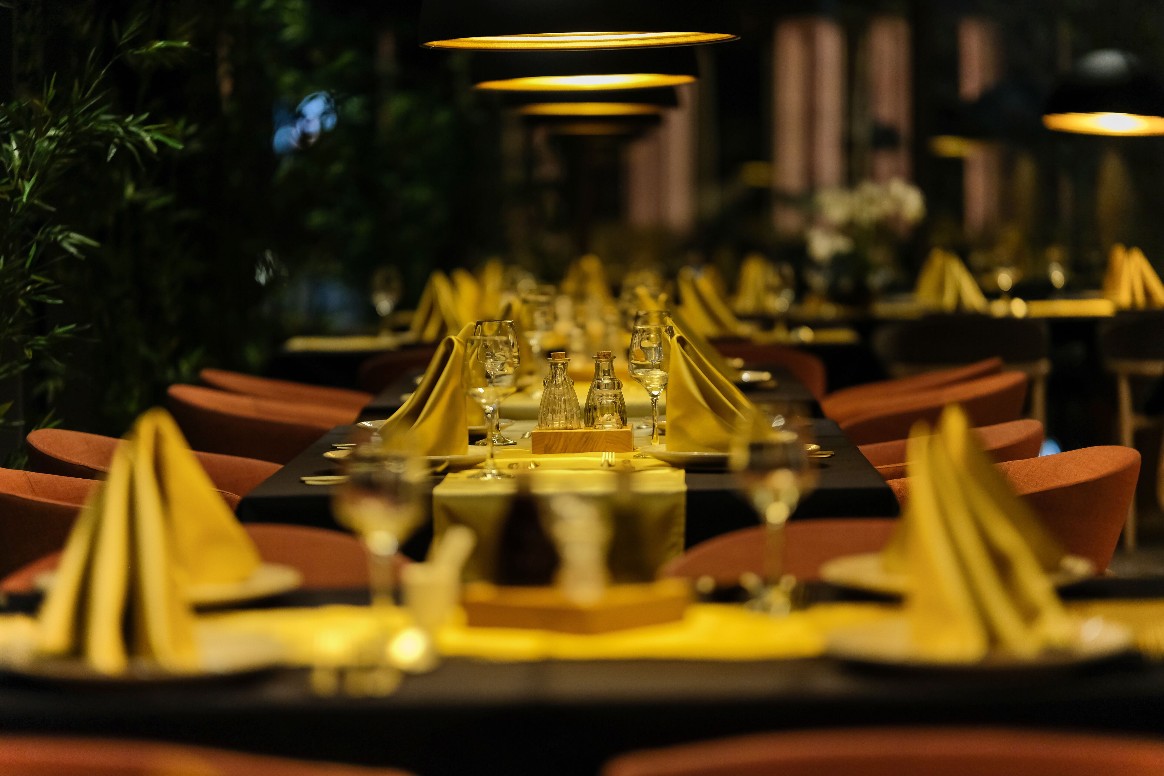 A long dining table with multiple chairs, each with a yellow napkin and a glass.
