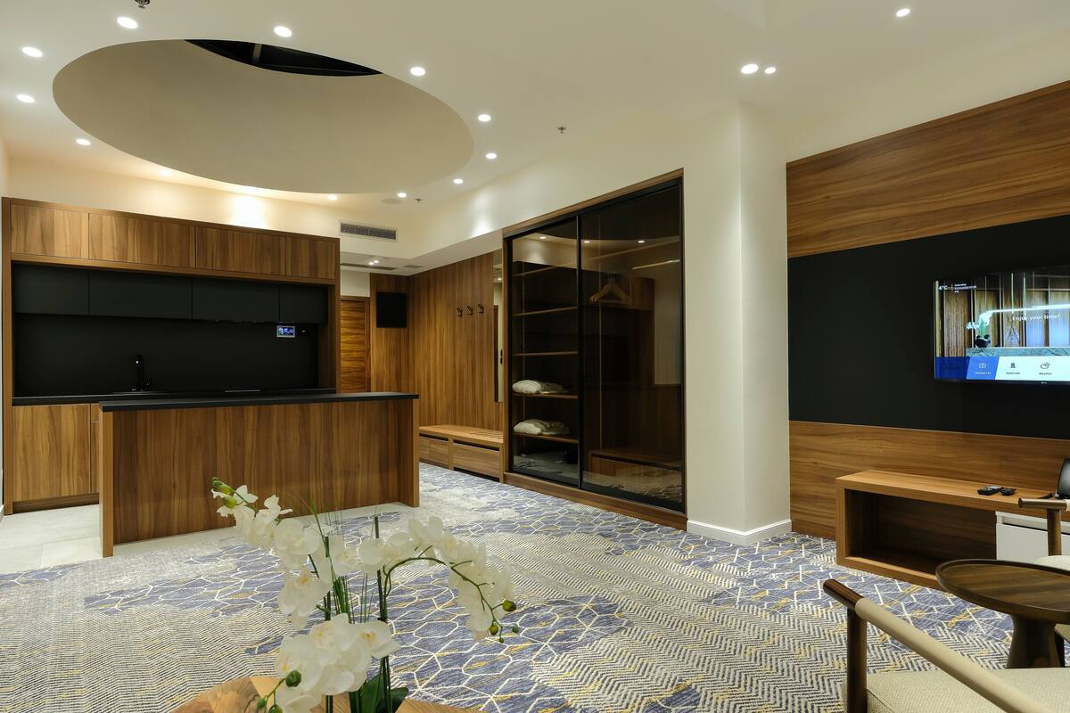 A modern hotel room with a wooden reception desk, a flat-screen TV, a walk-in closet, and a patterned floor.