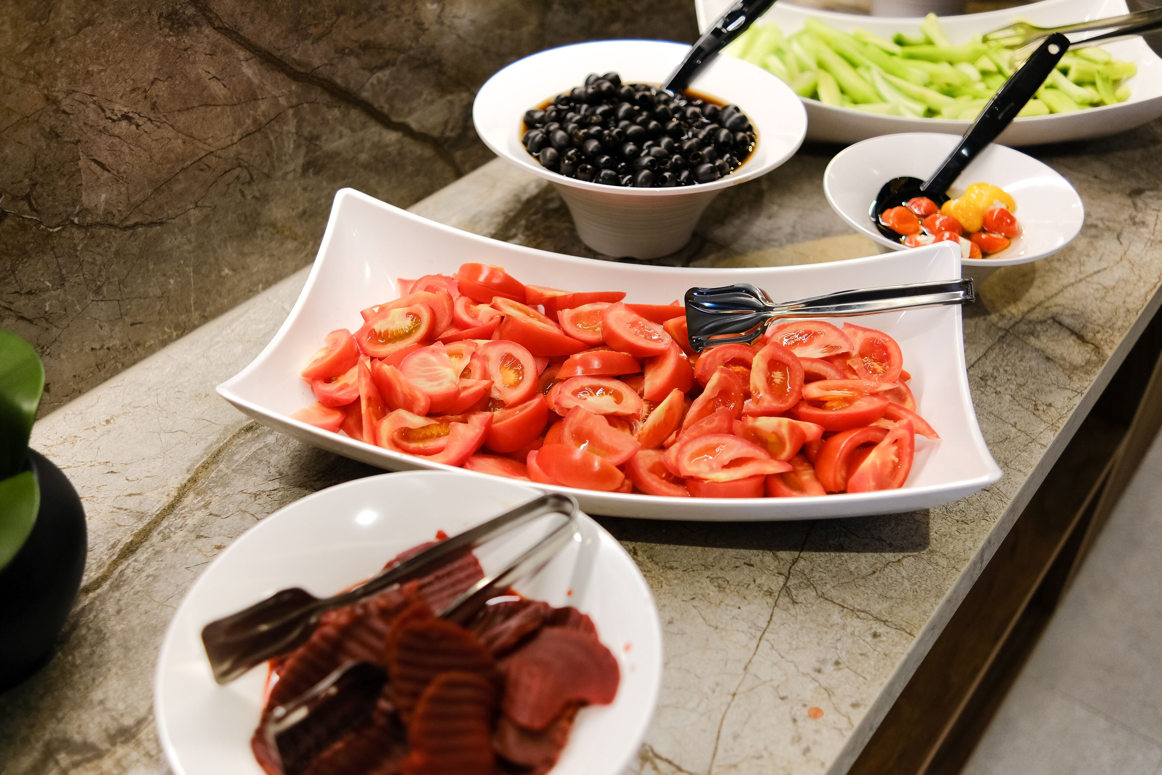 A buffet with various food items including sliced tomatoes, black beans, and green vegetables.