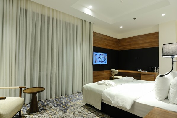 Una habitación de hotel moderna con una cama, una mesita, una silla, un televisor y un escritorio con lámpara.