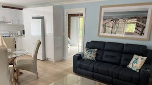 A modern living room with a glass coffee table, a black sofa with patterned cushions, and a dining area with a glass table and chairs.