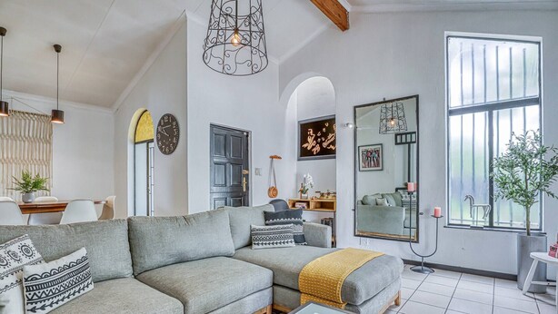 Un salon moderne avec un canapé d’angle, un coin repas comprenant une table et des chaises, une grande fenêtre offrant une belle vue et un miroir décoratif.