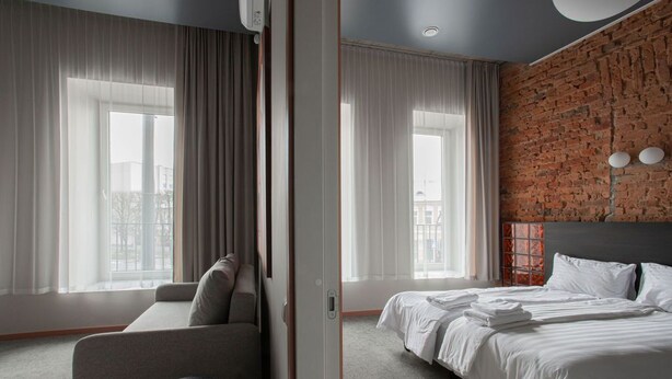 A hotel room with a brick wall, a large bed, a sofa, and a small round table.