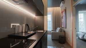 A modern hotel room with a kitchenette, a sofa, a bed, and a large window.