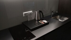 A modern kitchen with a built-in induction cooktop, a stainless steel kettle, a sink, and a coffee maker.