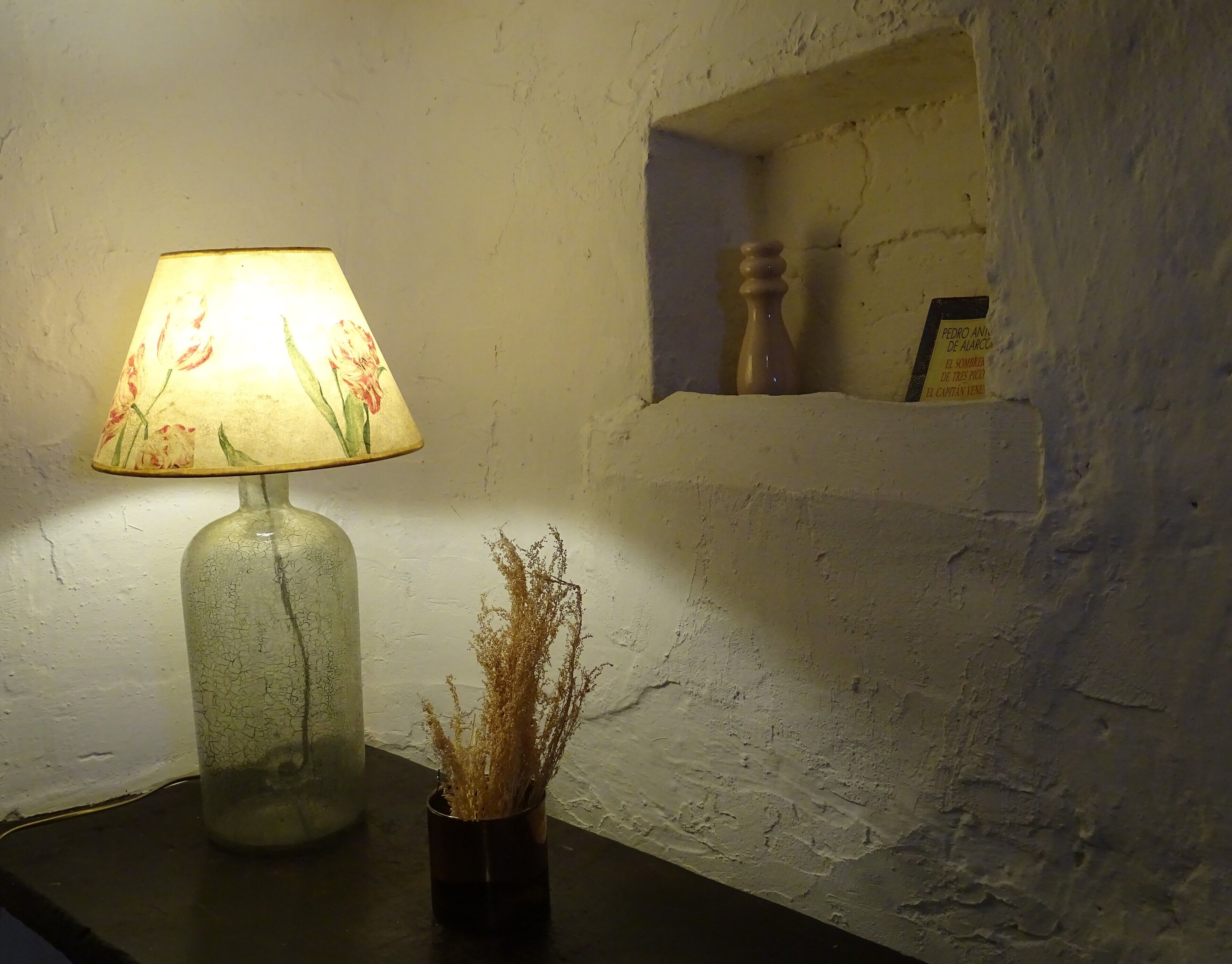 A lamp with a floral shade on a table next to a vase with dried plants.