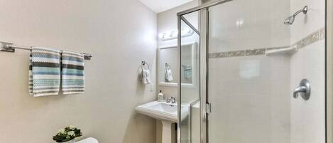 Et badeværelse med toilet, vask og brusekabine med glasvægge.
