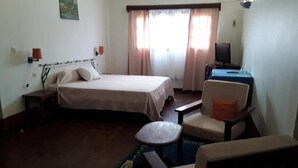 A hotel room with a bed, a desk, a chair, and a small table. - Hotel le Colbert (Antsiranana)