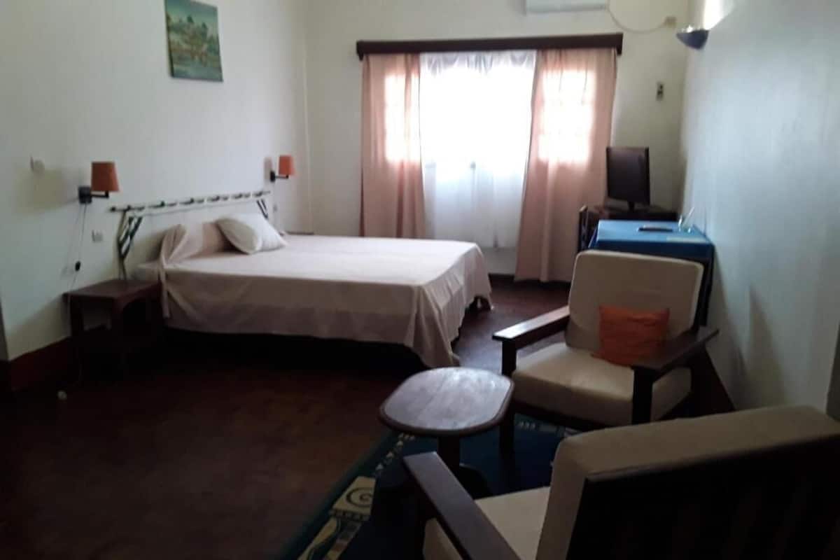 A hotel room with a bed, a desk, a chair, and a small table.