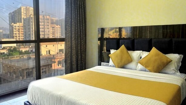 Una habitación de hotel con un ventanal grande, una cama con cabecera y vistas a edificios.