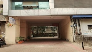 Entrada de un edificio con un vestíbulo cubierto, plantas en macetas y un cartel.