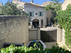 A courtyard with a stone wall, a small pool, and a building with a star decoration and green shutters. - Cosy village house in Provence for 2,4,6 or 8, air-con, courtyard with swim pool (Eygalières)